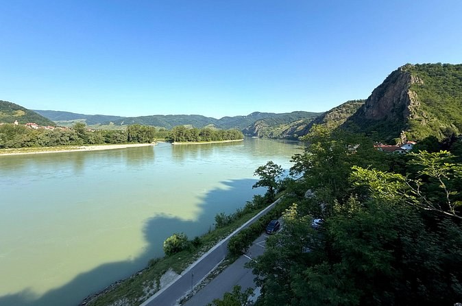 The Danube below a rocky, wooded crag, with a riverside road and cycle path
