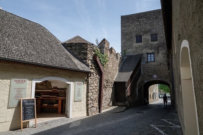 A stone gate tower beside a Wieser Wachau shop on a cobbled lane