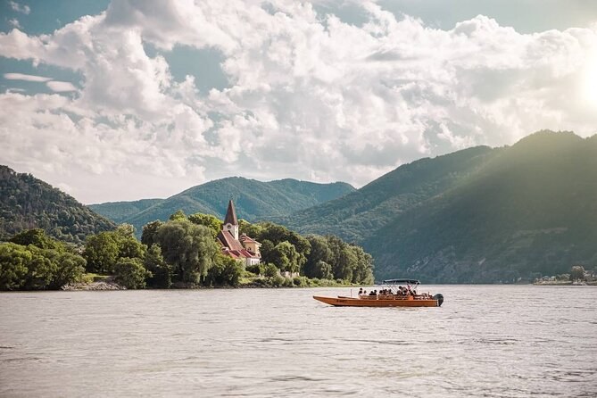 A wooden boat on the Danube below a church among the trees and the wooded hills